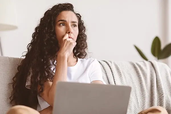 A woman at her laptop looking worried and biting her fingernails