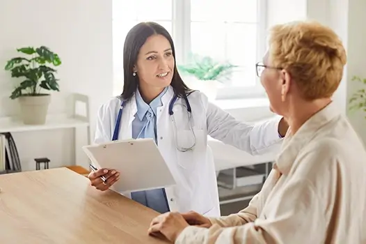 A doctor holding a clipboard and placing her hand on a patients shoulder