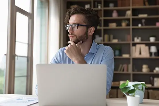 A man sitting at his laptop and looking outside distractedly