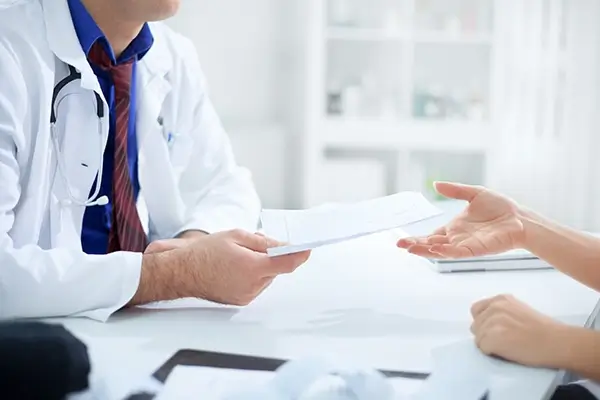 A physician and a patient exchanging papers at a table