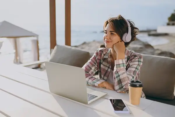 A smiling woman sitting outside with a laptop and a coffee