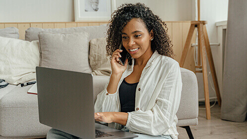 A lady on her phone and looking at her laptop, smiling.