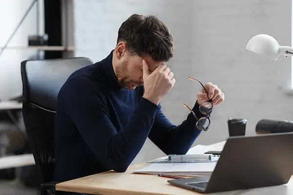 A man at his workstation rubbing his head